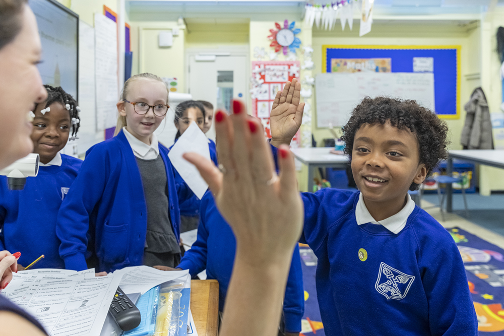 Children in classroom giving a teacher a high five